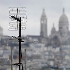 A tv antenna is seen on the rooftops of residential buildings in front of the Sacre Coeur