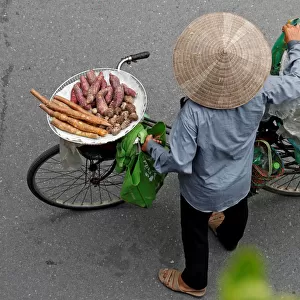Vietnamese woman transports cooked cassava and potato for sale by a bicycle on a street