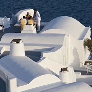 Greece, Santorini, Thira, Oia. Two couples are served for dinner at white villa overlooking sea
