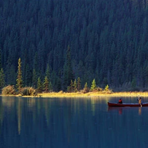 Two people paddle in a canoe in the early morning light, with lush forest behind them
