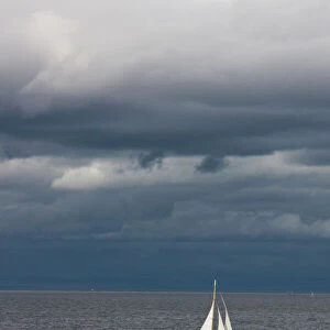 A small sailboat makes its way through the waters of Puget Sound under dark storm clouds