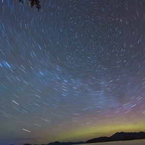 US, AK, Ketchikan. Northern Lights glow on horizon with star trails rotating around North Star