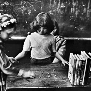 Two 5th grade girls playing jacks on the teachers desk before school in Clairfield, Tennessee. Photograph by Jack Corn, 1964