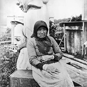 ALASKA: ESKIMO WOMAN. A seated Eskimo woman with totem pole sculptures behind her