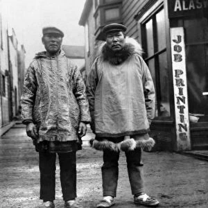 ALASKA: ESKIMOS. Two Eskimo men standing on a commercial street with shops in the background