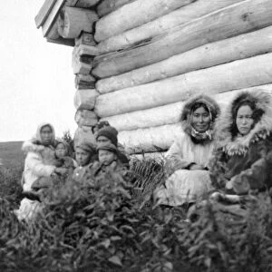 ALASKA: ESKIMOS. A group of Eskimo women and children sitting in front of a log