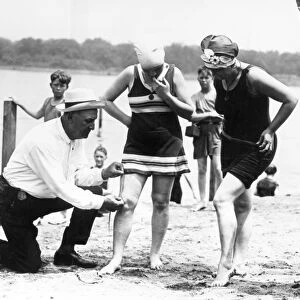 BATHING SUITS, 1922. A Public Buildings and Grounds officer measures womens bathing suits to ensure they are not more than six inches above the knee, Washington, D. C. 1922
