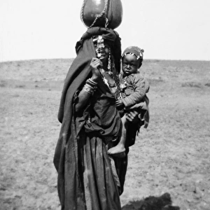 BEDOUIN WOMAN & CHILD. A Bedouin woman carrying a child and a water jug, from Beersheba, Israel