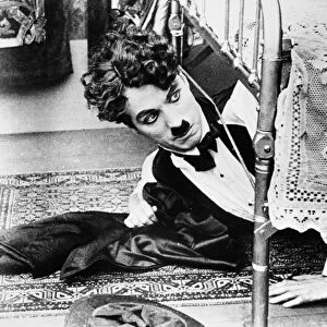 CHARLIE CHAPLIN (1889-1977). Charles Spencer Chaplin. English comedian. Getting out from under the bed in one of his silent movies from the 1920s