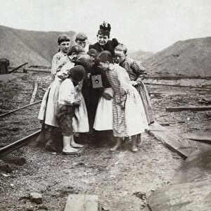 CHILDREN WITH CAMERA, c1900. Group of children crowded around photographer Frances