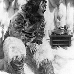 ESKIMO AND PHONOGRAPH. An Eskimo man sitting among furs listening to the phonograph