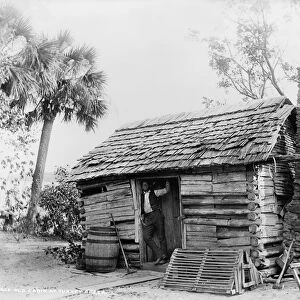 FLORIDA: LOG CABIN. An African American man standing in the doorway of a log cabin
