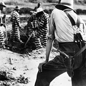 GEORGIA: PRISONERS, 1941. A prison guard watching convicts as they work in a prison camp in Oglethorpe County, Georgia. Photograph by Jack Delano, May 1941