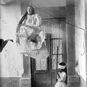 A girl swings at a Christmas pinata in Mexico, c1915