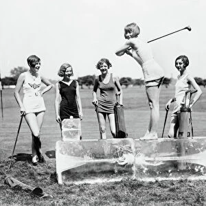 GOLFING, 1926. Women wearing bathing suits, teeing off from a block of ice on a golf course