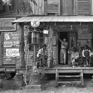 A group of African American men sitting on the porch of a country store, with the owners brother standing in the doorway, on a Sunday afternoon with a kerosene pump on the right and the gasoline pump on the left in Gordonton, North Carolina. Photograph by Dorothea Lange, July 1939. From the Farm Security Administration photography pr