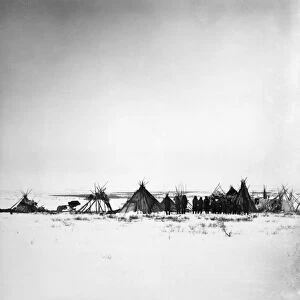 A group of Naskapi Native Americans standing next to tipis at a camp in Labrador, Canada, with a cache of furs and hides. Photographed by Lucien M. Turner, 1882