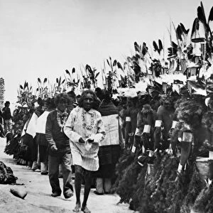 Hopi dancers, wearing Hemis Kachina masks and sprigs of evergreen, lined up at a pueblo in Arizona during the Niman Kachina or going home ceremony in the month of July. Photographed c1913