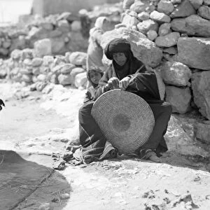 JORDAN: BEDOUIN WEAVING. A Bedouin woman weaving a straw mat, accompanied by two young boys