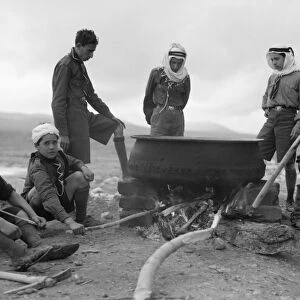 JORDAN: BEDOUINS, 1935. A group of Bedouins cooking in a large pot, in the Shunat