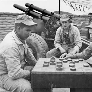 KOREAN WAR (1950-1953). The crew of a 105mm Howitzer with the First Marine Division play a game of checkers with artillery fuse caps: Cpl. Oswaldo Nira of Texas (left) and Pfc. Samuel B. Fielder of Maryland (right) consider their moves as a telephoneman looks on: photographed in Korea, 1952