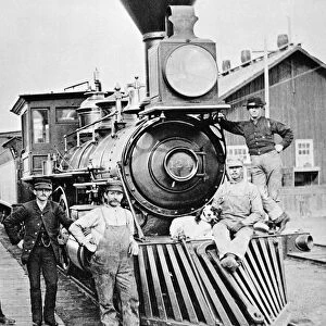 LOCOMOTIVE, 1883. The conductor, crew and canine mascot of a Central Pacific Railroad train posing by the locomotive during a station stop at Mill City, Nevada. Photographed in 1883