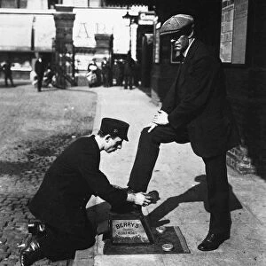 LONDON: BOOTBLACK, c1900. Bootblack at work outside the entrance to a railway station in London