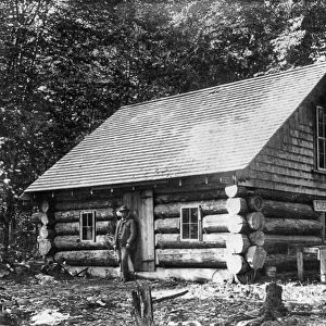 MAINE: LOG CABIN. A man standing in front of a log cabin at the Lucky Camp in Spencer Bay