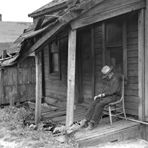MAN ON PORCH, 1936. Old Age. Old man taking a nap on the dilapidated porch of a run down home