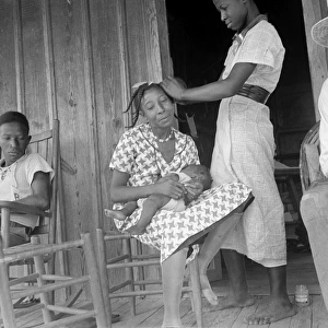 MIGRANT FAMILY, 1936. An African American woman braids another womans hair while