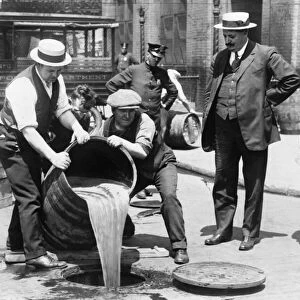 New York City Deputy Police Commissioner, John A. Leach (right), watches agents pour liquor into a sewer after a raid, c1921