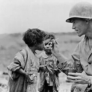 SOLDIER AND CHILDREN. An American soldier feeding a young child, probably during World War II