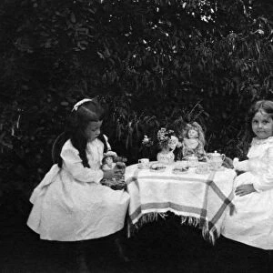 TEA PARTY, c1900. Two girls having a tea party with their dolls in a garden. Photograph