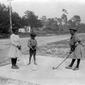 Three African American children playing golf with clubs made of sticks. c1905