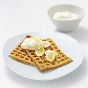 Belgian waffles served with whipped cream, banana slices and golden syrup, high angle view