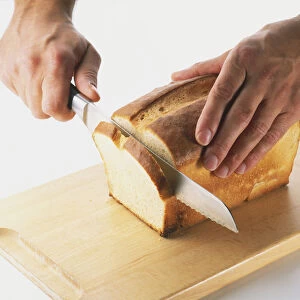 Close-up of slicing a loaf of white bread using a sharp serrated bread knife