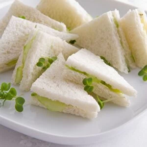 Cucumber sandwiches on white bread, served with watercress garnish on white plate, close-up