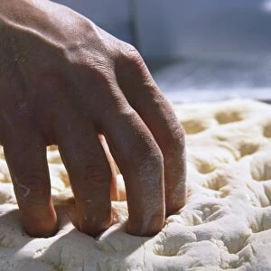 Fingers pressing holes into thick layer of fresh dough
