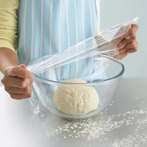 Girls hands covering bread dough in glass bowl with clingfilm