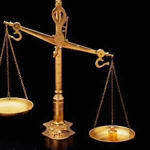 These are the golden Scales of Justice. They represent the legal system and courts. The scales here are shown unbalanced with the left side weighing heavier than the right. They are shown against a black background