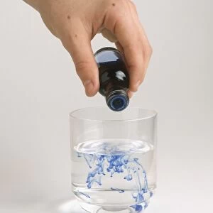 Hand pouring food colouring into glass of water