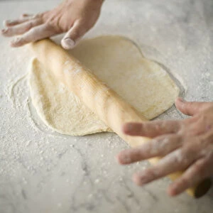 Hand rolling out pizza dough with rolling pin, close-up