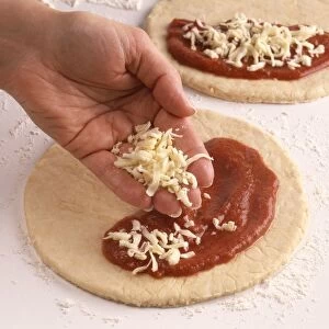 Making calzone pizza, sprinkling cheese on top of tomato sauce on pizza base