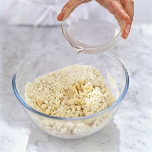 Pouring water over dry puff pastry in glass mixing bowl