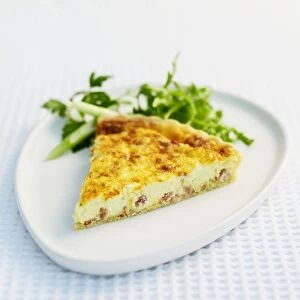 Slice of quiche Lorraine served on white plate with salad greens