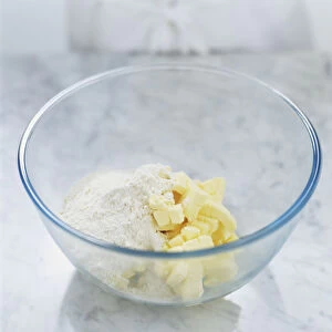 White flour and butter cubes in a glass bowl, close up