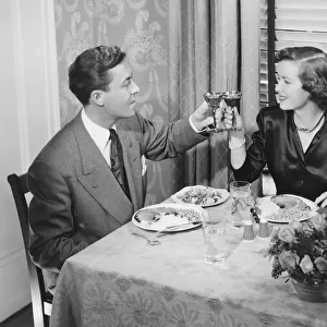 Couple toasting at dinner table, (B&W), elevated view