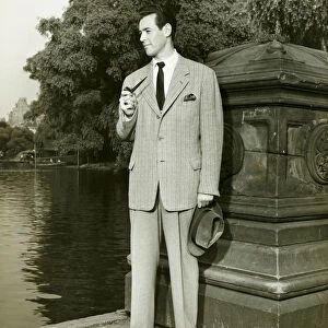 Elegant man smoking pipe by park lake, (B&W), portrait