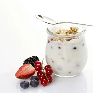 Glass and spoon with muesli, yoghurt, berries, red currants, blueberries, strawberry, blackberry