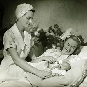Mother lying in bed smiling to baby-child (0-6 months), nurse standing beside, (B&W)